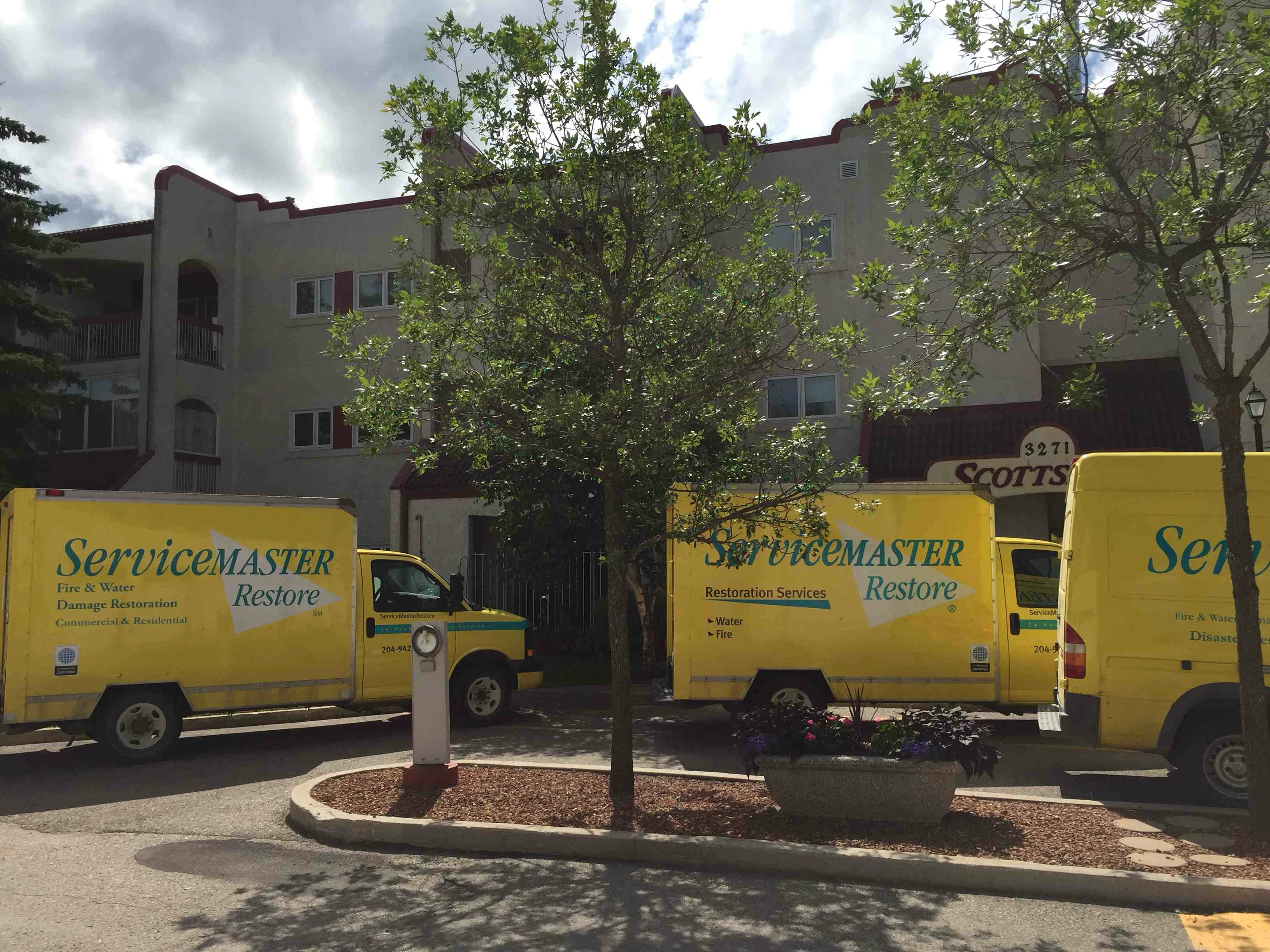 Three-yellow-ServiceMaster-vehicles-outside-apartment-building